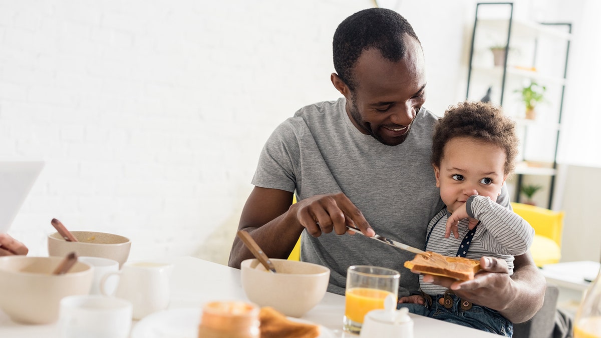 a father spreads peanut butter on his young son's toast