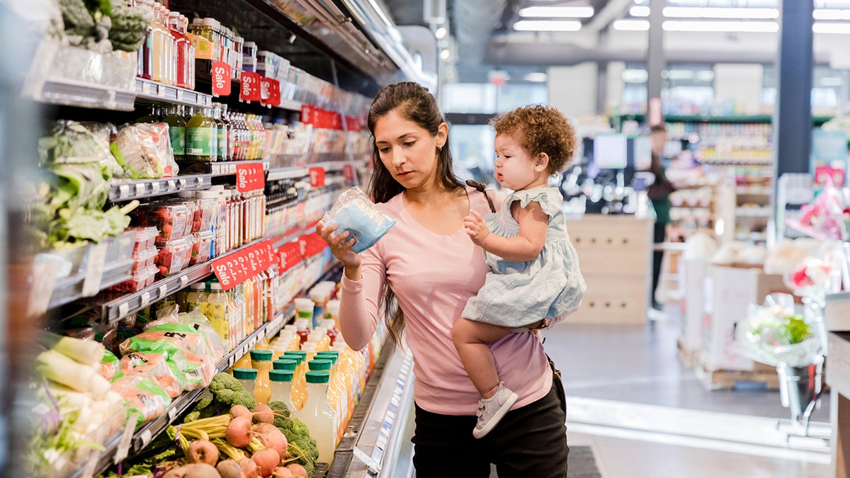 A young mother holds her daughter on her hip while grocery shopping